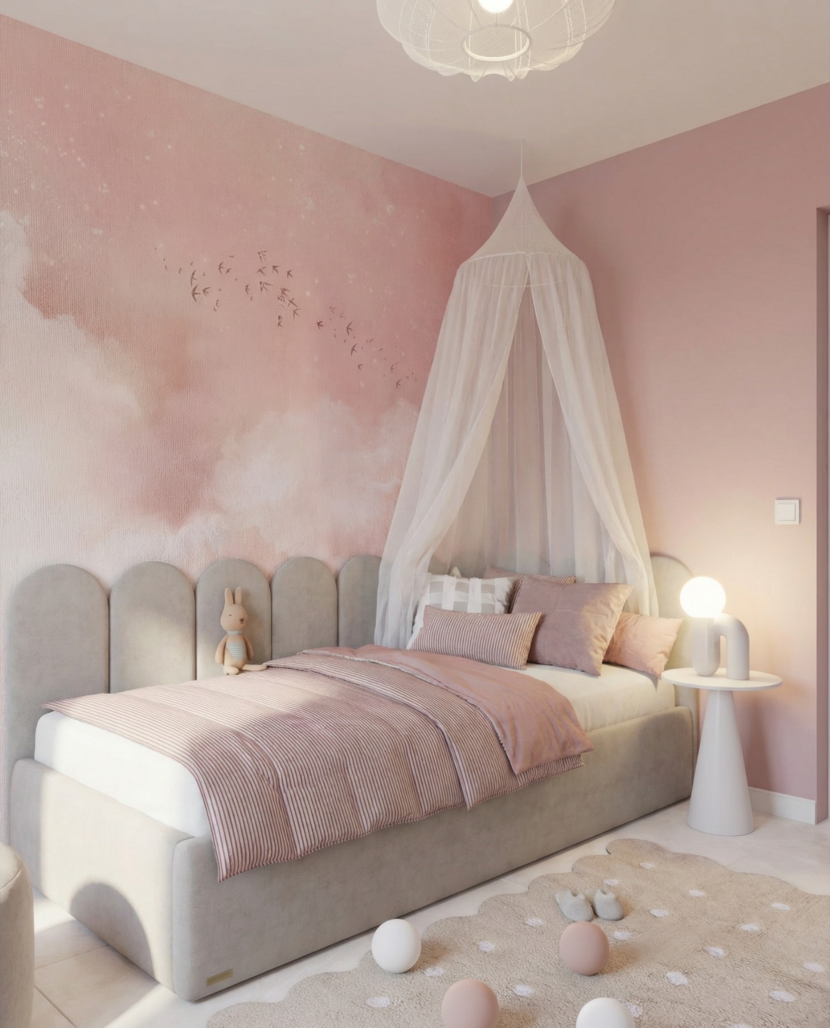 Pokój dziecięcy w odcieniach różu z łóżkiem, baldachimem i tapetą w chmury. Na łóżku leżą poduszki i kołdra w paski. Na podłodze dywanik w kształcie chmury i dekoracyjne kule.