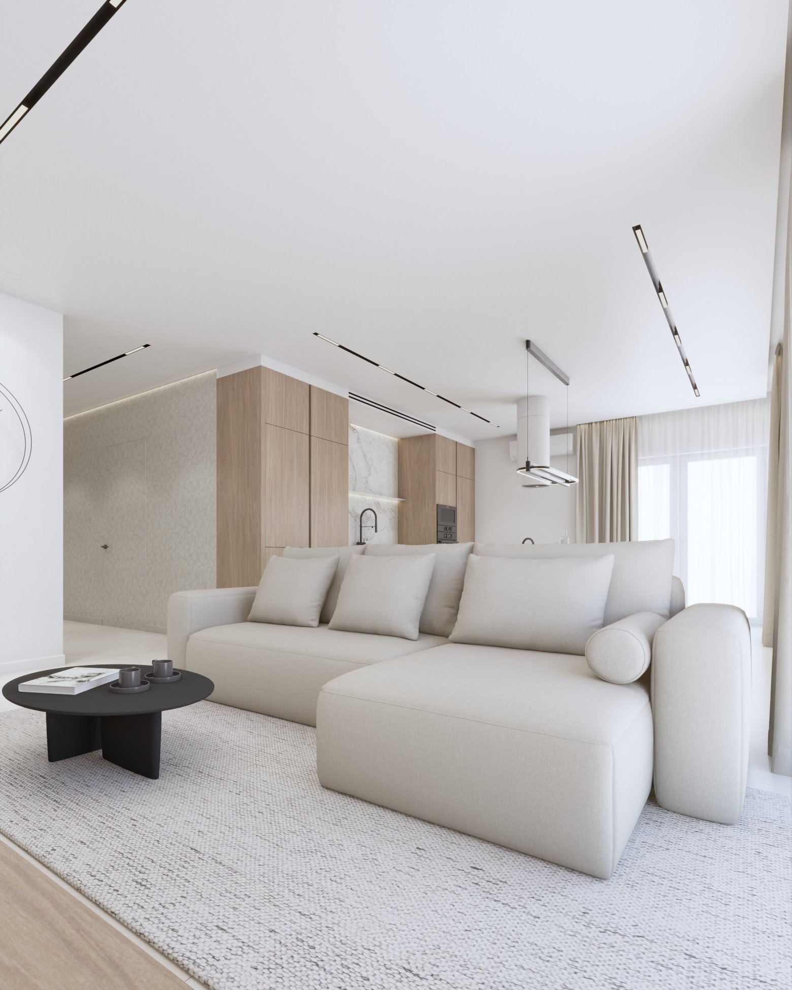 Jasne wnętrze z narożnikiem i okrągłym stolikiem kawowym. W tle zabudowa kuchenna z drewnianymi frontami i marmurowym blatem. Minimalistyczne oświetlenie sufitowe.