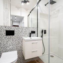 FHM Inżynieria Patrycja Wajdyk - Nowoczesna łazienka z kabiną prysznicową typu walk-in, umywalką na szafce i mozaiką na ścianie. Minimalistyczny design z czarnymi akcentami i jasnymi płytkami.