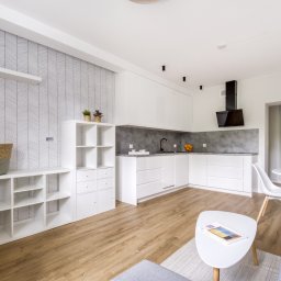 FHM Inżynieria Patrycja Wajdyk - Jasne, przestronne wnętrze: biała zabudowa kuchenna z szarym blatem, drewniana podłoga, wzorzysta tapeta i minimalistyczne meble w salonie. Nowoczesny design.