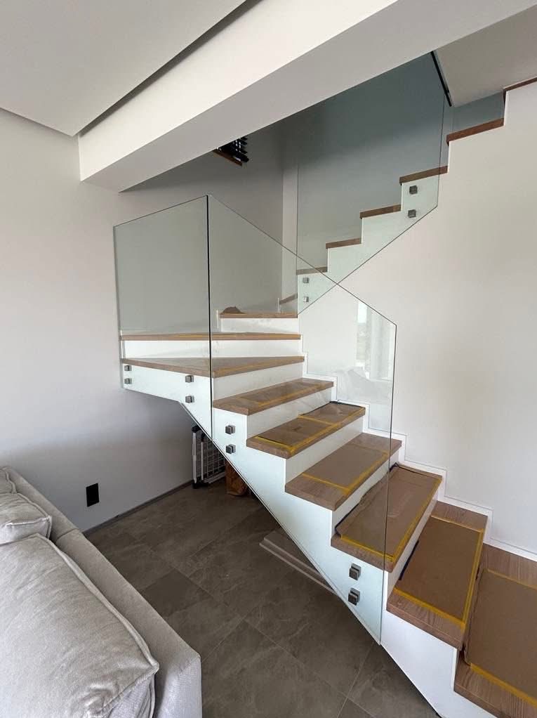 Nowoczesne schody z białymi stopnicami i szklaną balustradą, zabezpieczone kartonem. Minimalistyczny design, jasne wnętrze, widok z dołu na górę.