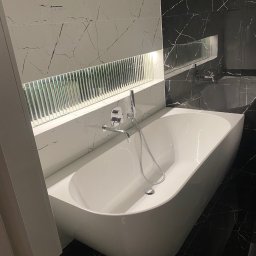 Wiesław Zwoliński - Nowoczesna łazienka z białą wanną wolnostojącą i czarno-białymi płytkami imitującymi marmur. Nad wanną dekoracyjny element z podświetleniem.