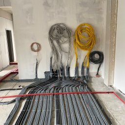Krzysztof Sobina - Szczegółowe ułożenie przewodów elektrycznych w peszlach, przymocowanych do podłoża w surowym wnętrzu. Widoczne kable zwinięte w pętle na ścianie.