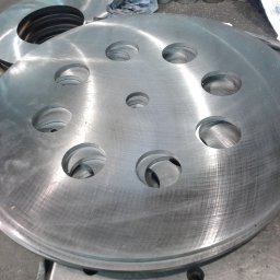 PPUH ZMETIS-BIS MAREK SOSNOWSKI - Stos metalowych dysków z otworami, obrobionych na tokarce. Widoczne ślady obróbki skrawaniem i narzędzia. Detal z bliska, surowy wygląd.