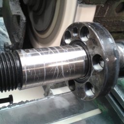 PPUH ZMETIS-BIS MAREK SOSNOWSKI - Obróbka tokarska metalowego wału z kołnierzem na tokarce. Widoczne ślady chłodziwa i gwintowany koniec wału.