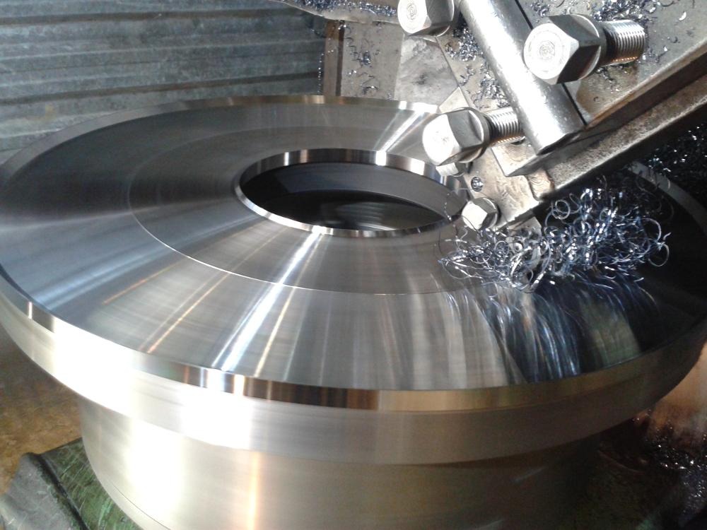 Obróbka metalu na tokarce: precyzyjne toczenie dużego, okrągłego elementu z otworem, wióry metalowe, narzędzie skrawające. Detal z połyskiem, widoczne ślady obróbki.