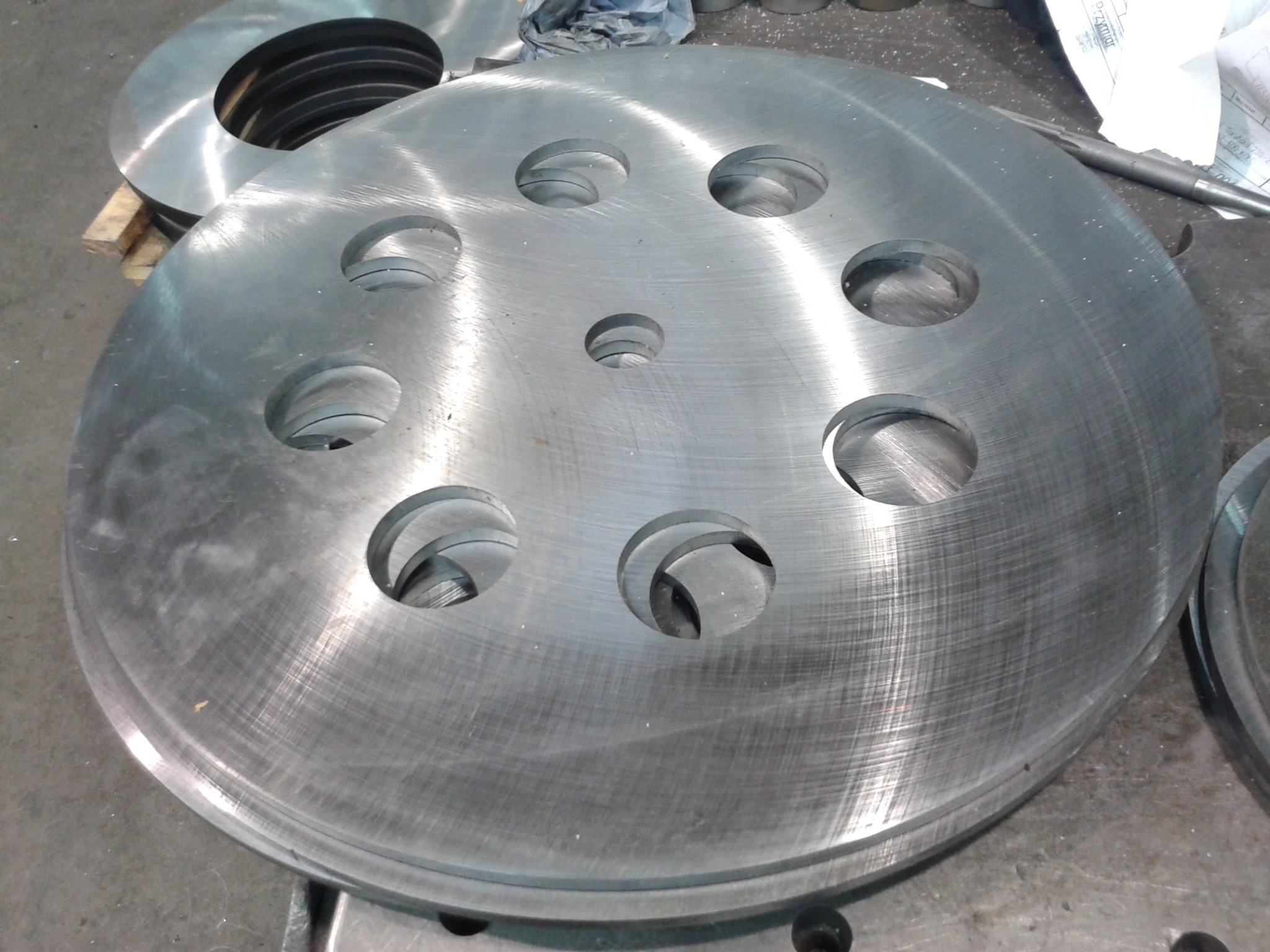 Stos metalowych dysków z otworami, obrobionych na tokarce. Widoczne ślady obróbki skrawaniem i narzędzia. Detal z bliska, surowy wygląd.