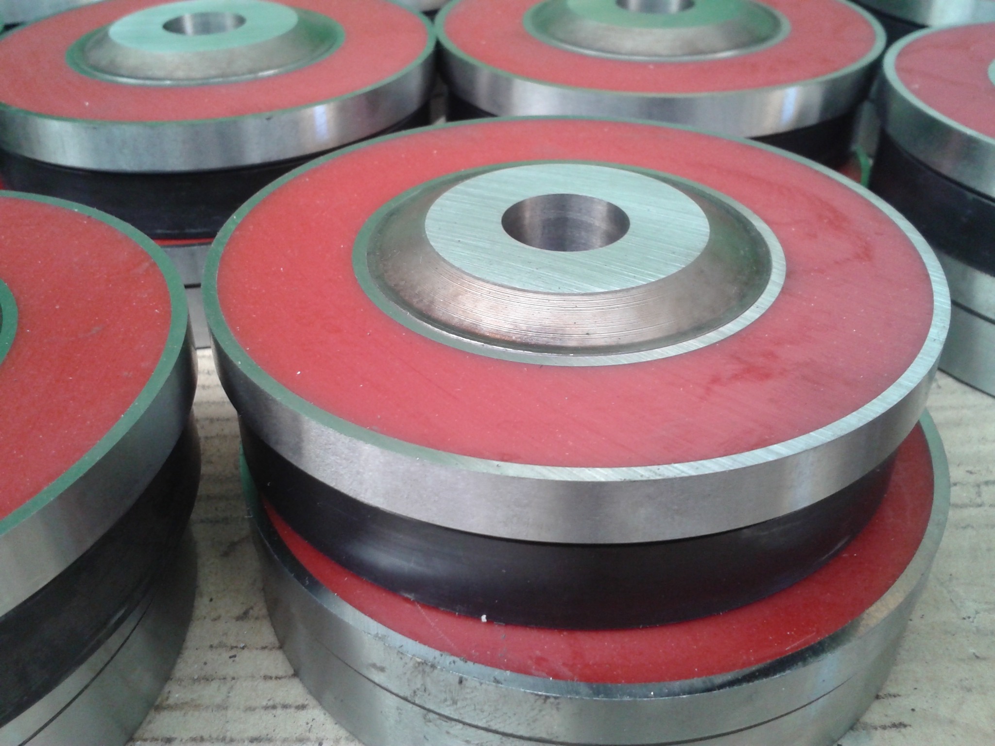 Metalowe elementy z czerwonymi i czarnymi wstawkami, ułożone jeden na drugim, tworzące okrągłe konstrukcje. Widoczne ślady obróbki.