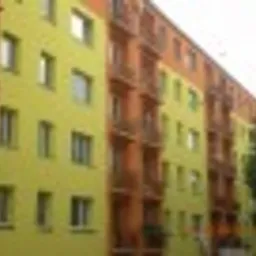 Wielorodzinny budynek po renowacji z żółtą elewacją i pomarańczowymi balkonami, widoczne detale architektoniczne i świeża kolorystyka.