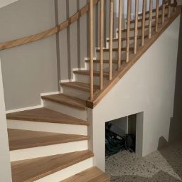 Projekt-Schody - Jasne schody drewniane z prostą balustradą z okrągłych belek, zintegrowane ze ścianą, z widocznym schowkiem pod spodem i posadzką lastryko.