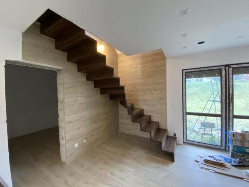 Nowoczesne, drewniane schody wiszące w jasnym wnętrzu domu w Łomiankach. Minimalistyczny design, drewno w ciepłym odcieniu, widok z dołu na konstrukcję.