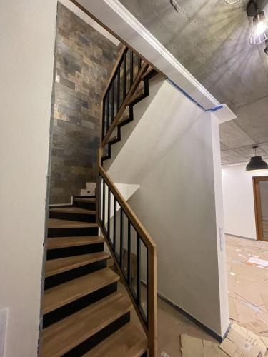 Nowoczesne schody z drewnianymi stopniami i czarną balustradą, widok z dołu, surowy betonowy sufit, kartony na podłodze, wnętrze w trakcie wykończenia.