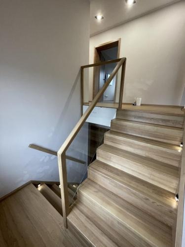 Jasne, drewniane schody z podświetleniem LED i szklaną balustradą z drewnianą poręczą, widok z dołu, nowoczesny design, oświetlenie sufitowe.