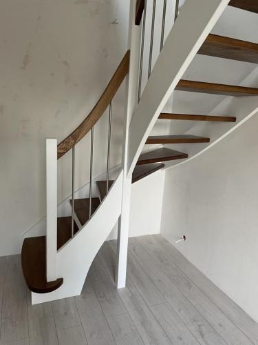 Bieg schodów z drewnianymi stopniami i balustradą z białymi elementami oraz stalowymi prętami, widok z dołu, jasne wnętrze.