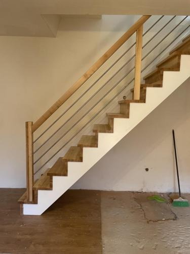 Nowoczesne schody z drewnianymi stopniami i balustradą z metalowych prętów. Widoczne niedokończone wykończenie podłogi i ściany. Ujęcie z dołu, perspektywa z boku.