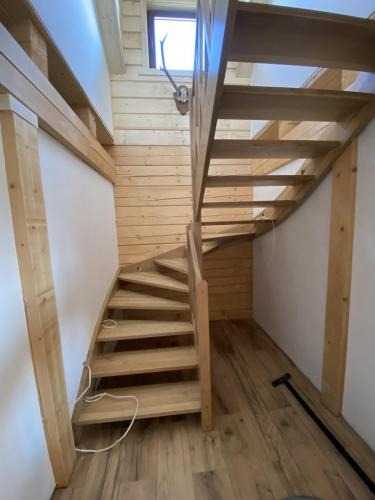 Drewniane schody spiralne w jasnym wnętrzu z boazerią i trofeum myśliwskim. Naturalne oświetlenie podkreśla strukturę drewna i minimalistyczny design.