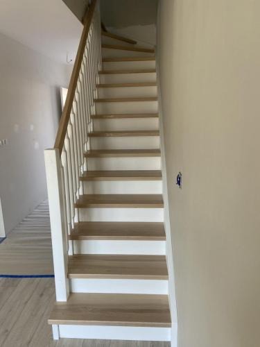 Jasne, drewniane schody z białą balustradą w nowoczesnym wnętrzu. Widok z dołu, ukazujący detale stopni i minimalistyczny design. Świeżo wykończone.