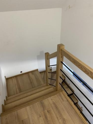 Jasne schody z drewnianymi stopniami i balustradą z czarnymi, poziomymi prętami, widok z góry, oświetlenie naturalne, minimalistyczny design.