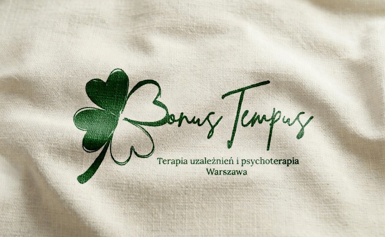 Logo Bonus Tempus z zieloną koniczyną na kremowym tle tkaniny, oferujące terapię uzależnień i psychoterapię w Warszawie. Elegancki font, subtelne cieniowanie.