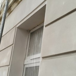 PARKER Budownictwo - Elewacja budynku po renowacji z oknem zabezpieczonym folią i fragmentem rusztowania. Jasna kolorystyka, wyraźne detale architektoniczne.