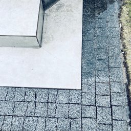 Deepwashservice Mycie ciśnieniowe - Szara kostka brukowa granicząca z jasnymi płytami tarasowymi i trawnikiem. Widok z góry, ukazujący detale faktury i połączenia materiałów.