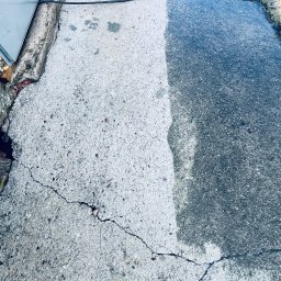 Deepwashservice Mycie ciśnieniowe - Efekt czyszczenia kostki brukowej: połowa powierzchni jest szara i brudna, a druga połowa jaśniejsza i czysta. Widoczne pęknięcia na kostce i fragment roweru.