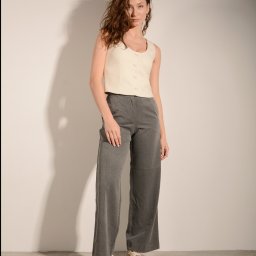 Anna Jachimczak - Portret kobiety w beżowej kamizelce i szarych spodniach na tle jasnej ściany. Ujęcie w pełnej sylwetce, z delikatnym oświetleniem i naturalną mimiką.