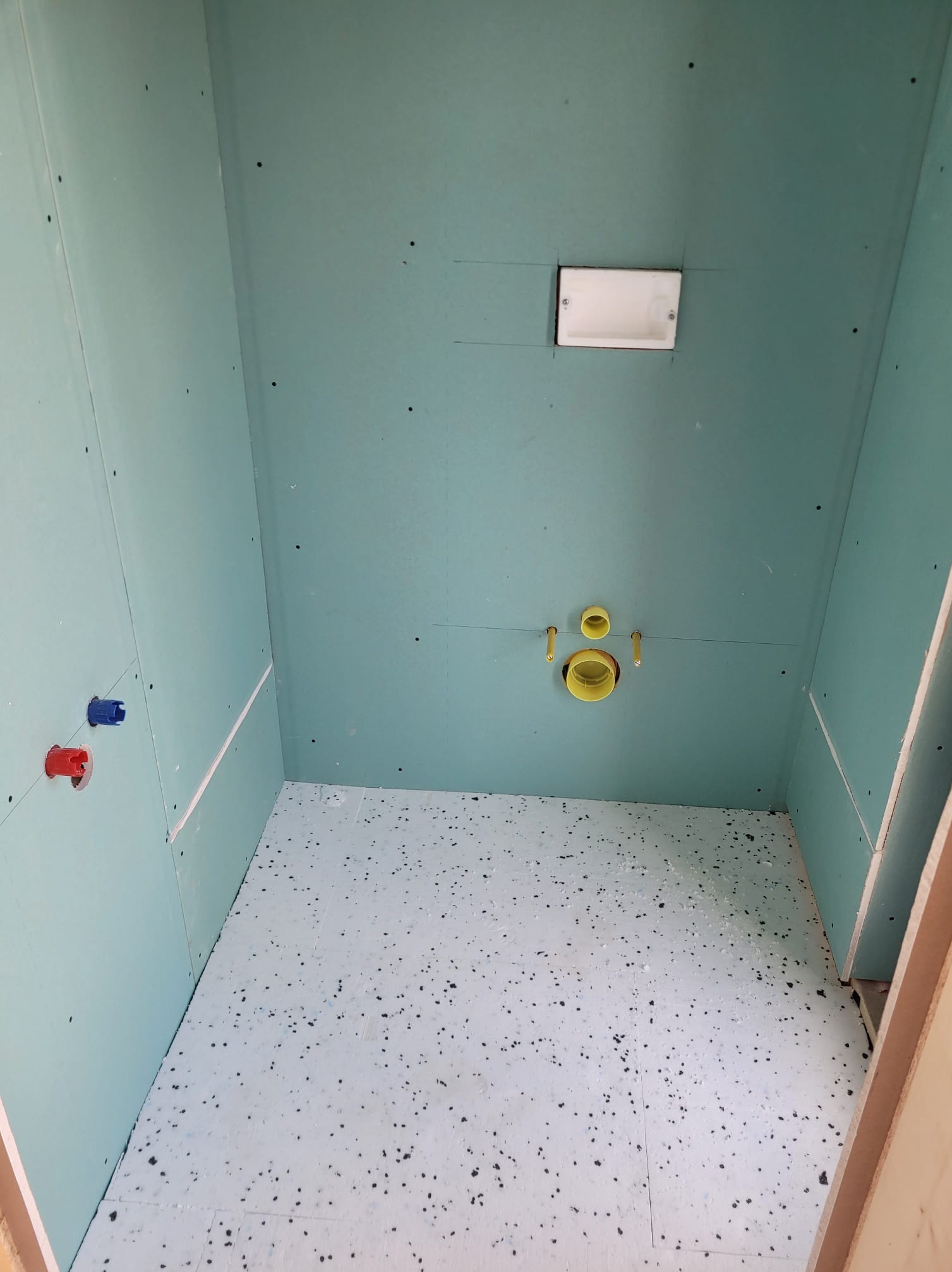 Łazienka w trakcie prac: ściany obłożone płytami kartonowo-gipsowymi, widoczne instalacje wodne i kanalizacyjne, podłoga przygotowana pod dalsze prace wykończeniowe.