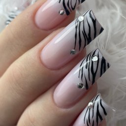 Saska Nails - Dłoń z kwadratowymi paznokciami w odcieniach różu, zdobionymi wzorem zebry i cyrkoniami, na tle białych piór. Efektowny i modny design.