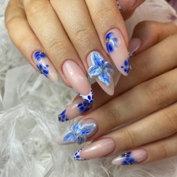 Saska Nails - Delikatne, beżowe paznokcie w szpic zdobione niebieskimi kwiatami 3D i wzorem w kropki, podkreślone złotymi akcentami na tle białych piór.