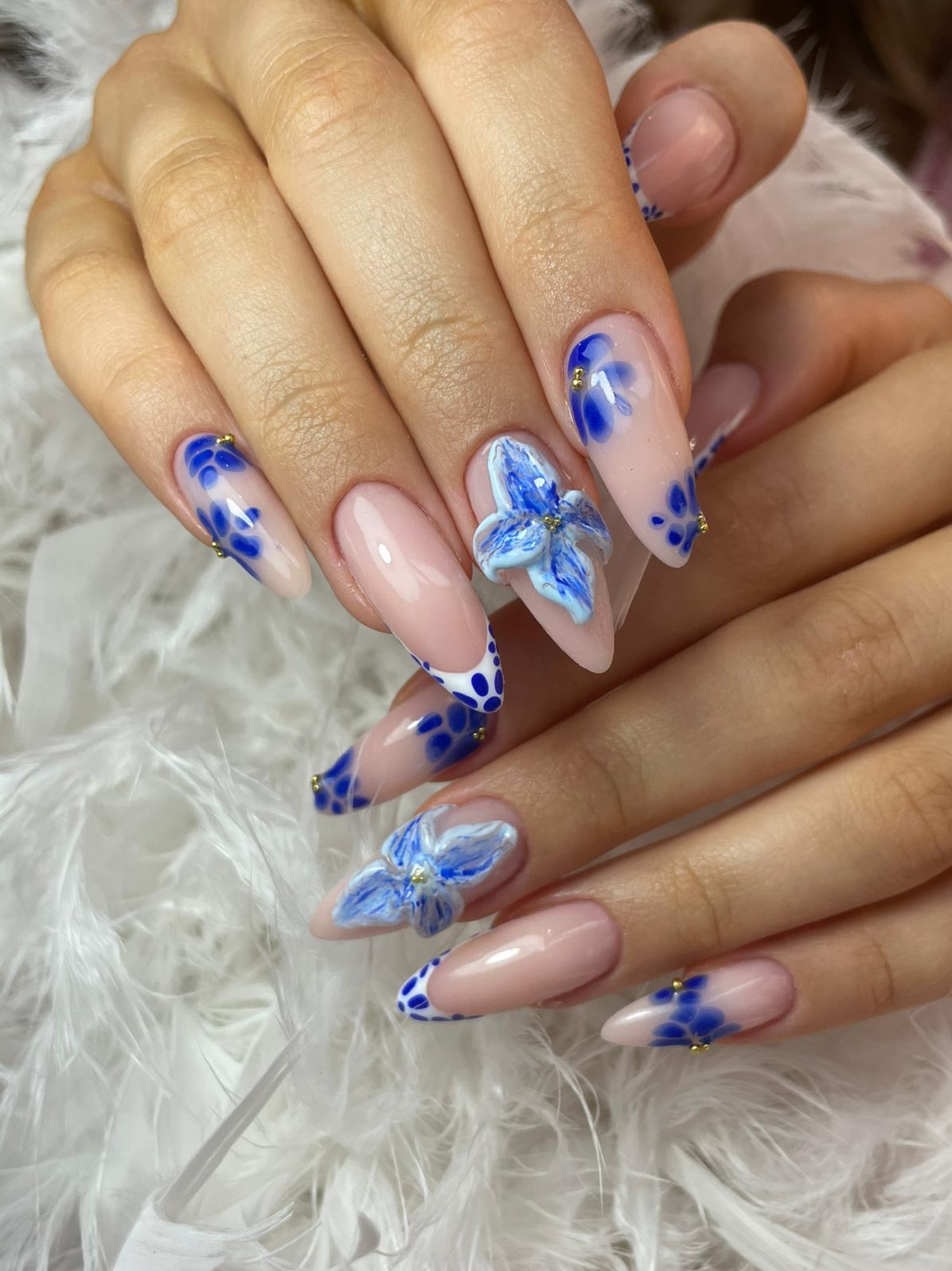 Delikatne, beżowe paznokcie w szpic zdobione niebieskimi kwiatami 3D i wzorem w kropki, podkreślone złotymi akcentami na tle białych piór.
