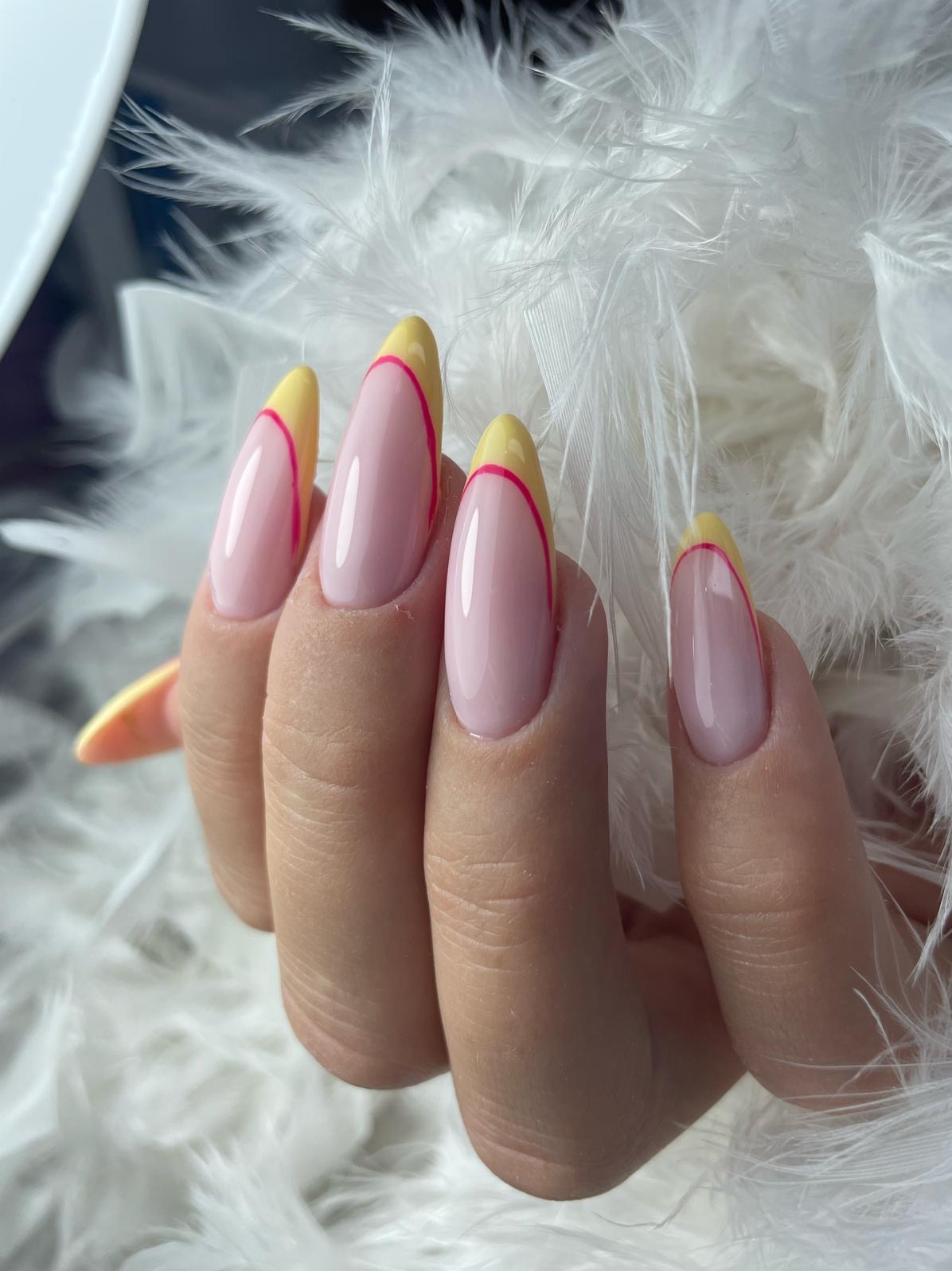 Dłoń z pastelowym manicure: beżowe paznokcie z żółtymi końcówkami i różową obwódką, na tle białych piór. Elegancki i nowoczesny design.