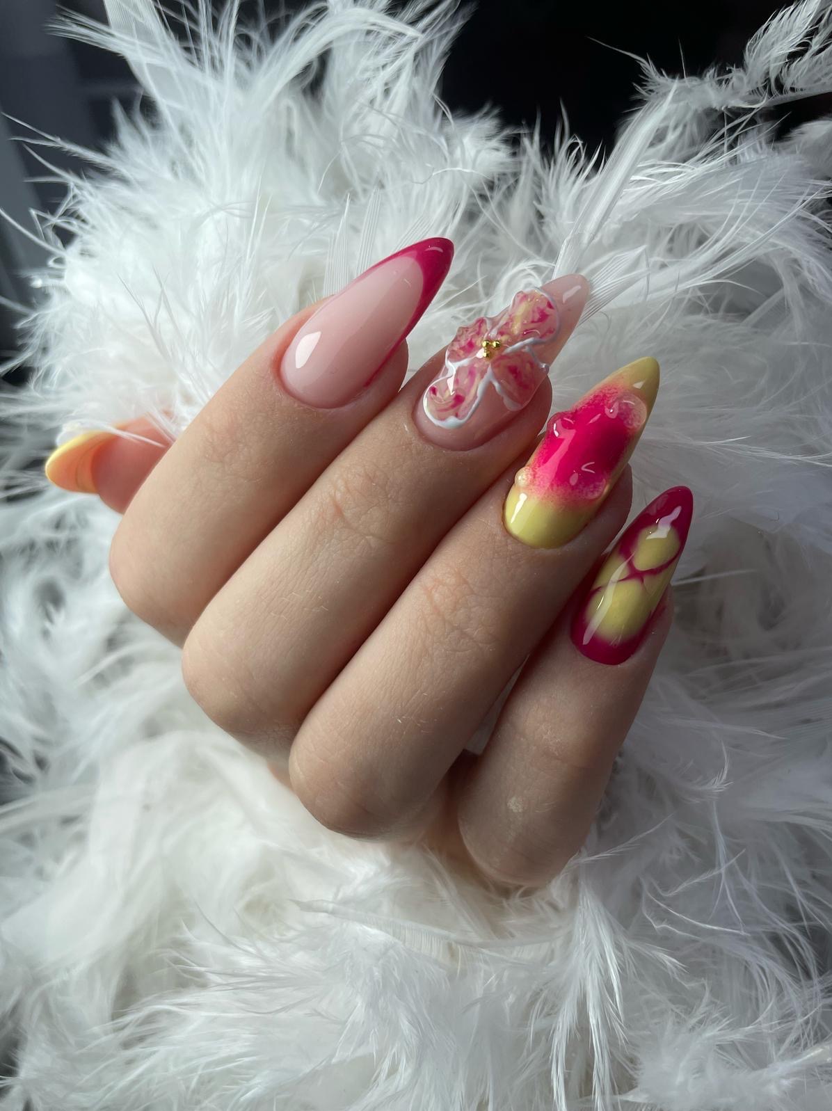 Efektowny manicure żelowy z kwiatowym zdobieniem i ombre w odcieniach różu i żółci, wykonany w Podegrodziu. Długie paznokcie na tle białych piór.