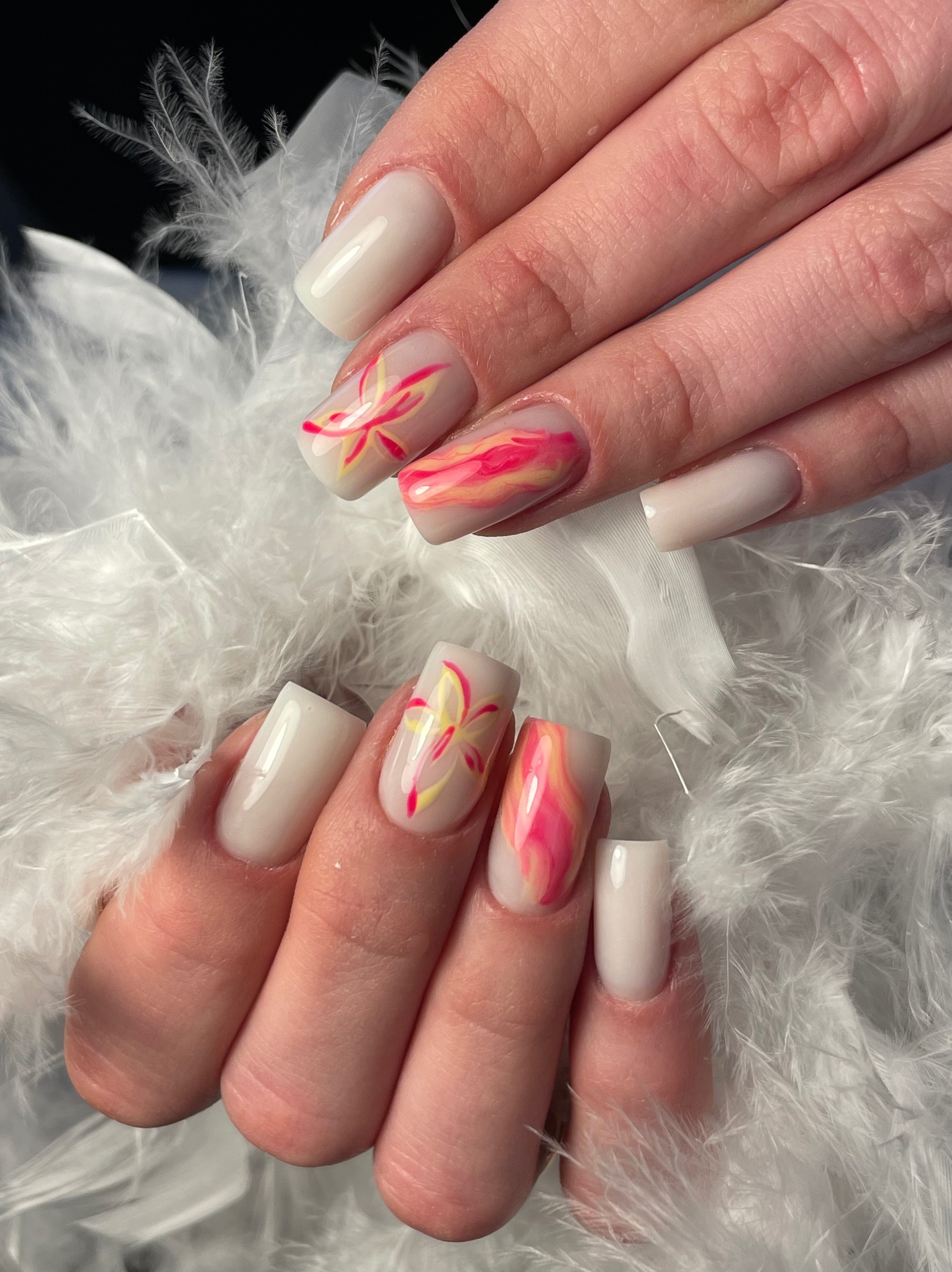 Dłonie z kwadratowymi paznokciami w odcieniach bieli, zdobione motywem kwiatowym i marmurkowym w różu i żółci, na tle białych piór. Efekt po zabiegu.