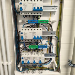 Rafał Barwikowski - Rozdzielnica elektryczna w białej obudowie z widocznymi bezpiecznikami, przewodami i listwami zaciskowymi. Instalacja wewnątrz skrzynki starannie ułożona.