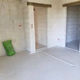 Rafał Barwikowski - Surowy stan wnętrza z widocznymi przewodami elektrycznymi w białych rurkach na ścianach z betonu komórkowego i podłodze. Widoczne otwory drzwiowe.