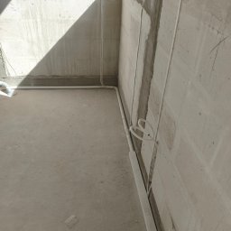 Rafał Barwikowski - Surowy stan: białe kable elektryczne prowadzone wzdłuż ścian w nowym budynku, widoczne puszki instalacyjne i betonowe ściany w trakcie prac wykończeniowych.