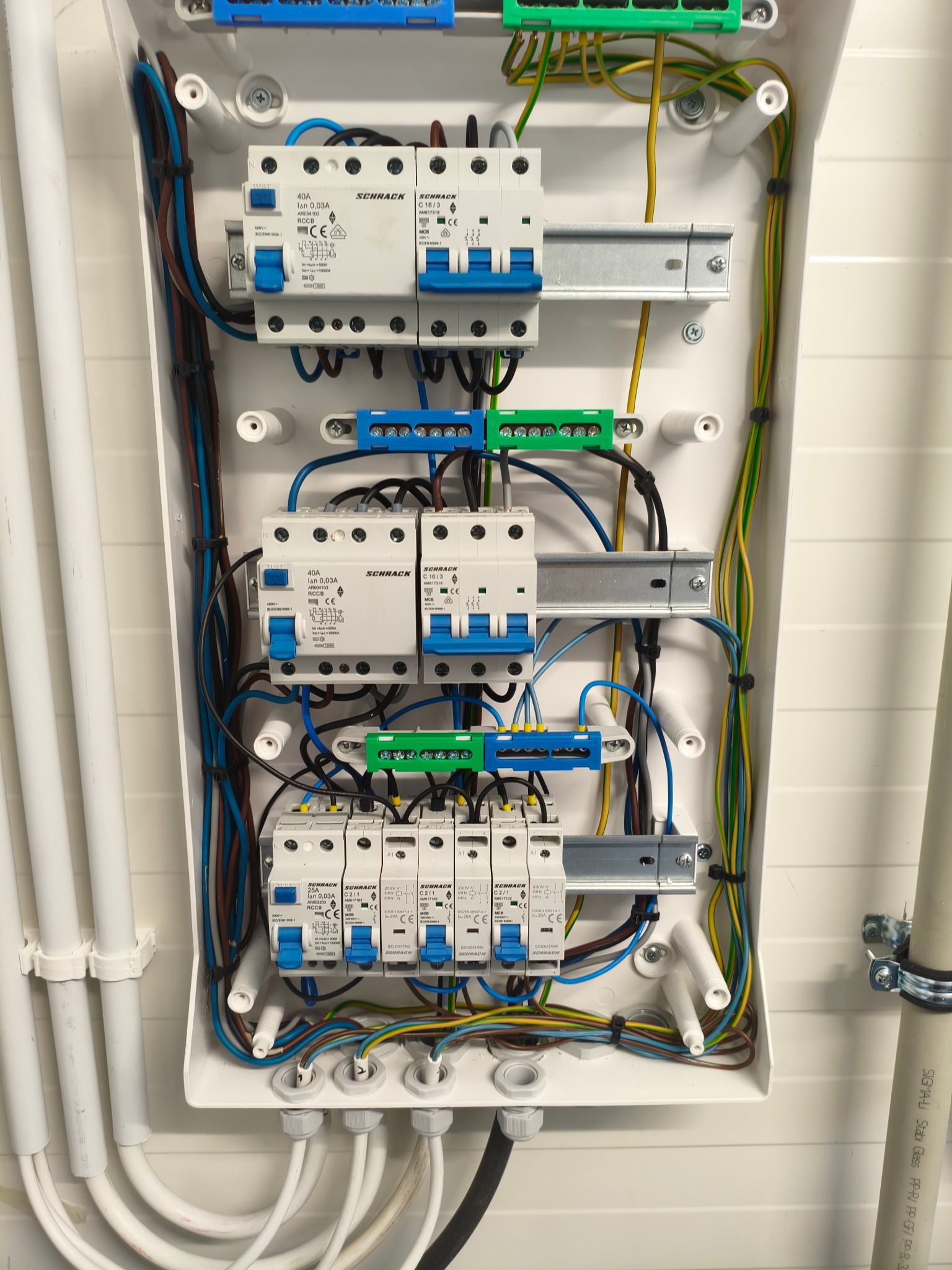 Rozdzielnica elektryczna w białej obudowie z widocznymi bezpiecznikami, przewodami i listwami zaciskowymi. Instalacja wewnątrz skrzynki starannie ułożona.