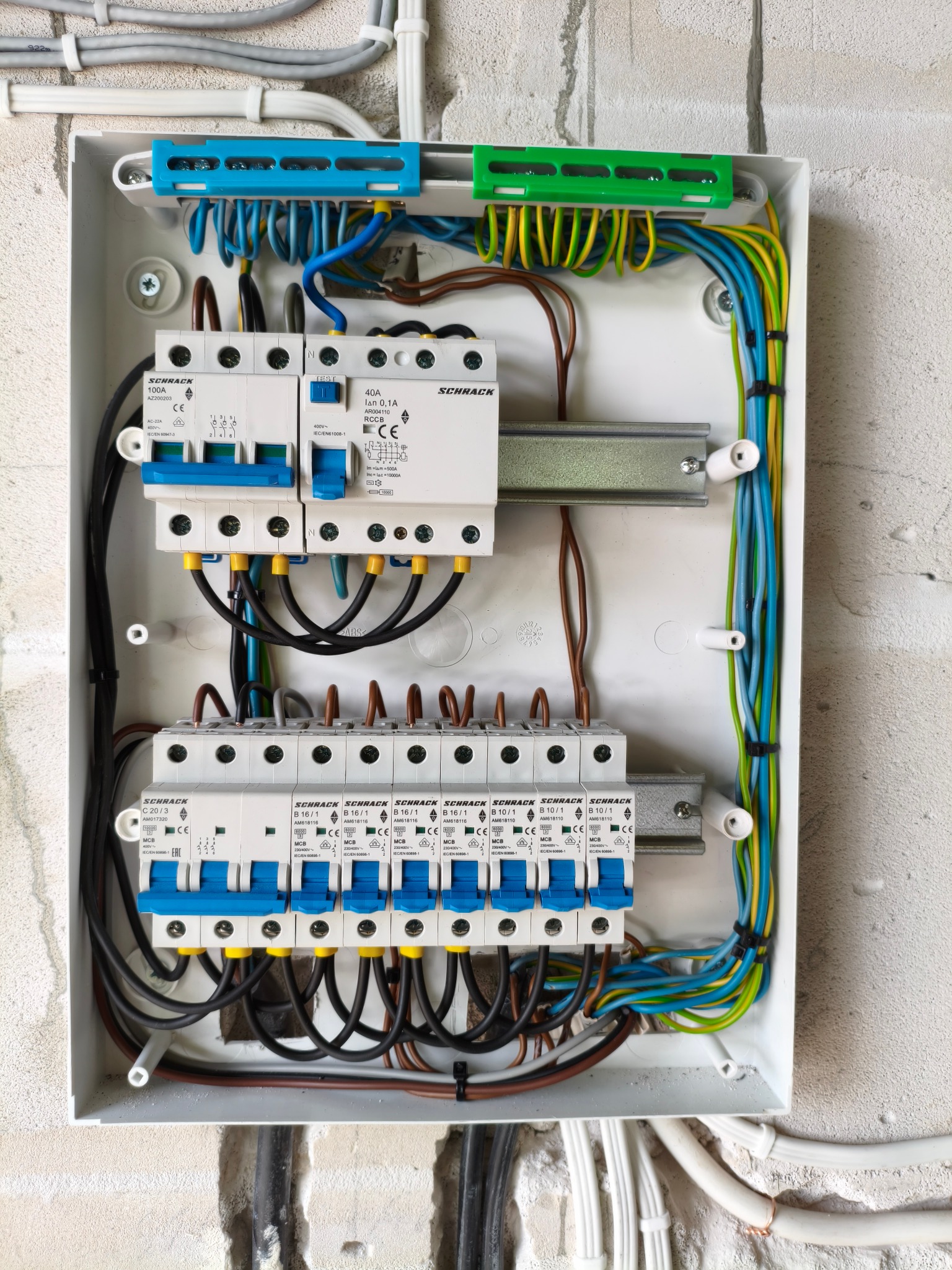 Rozdzielnica elektryczna Schrack z zainstalowanymi bezpiecznikami i okablowaniem, widok z góry. Instalacja w białej obudowie na tle surowej ściany.