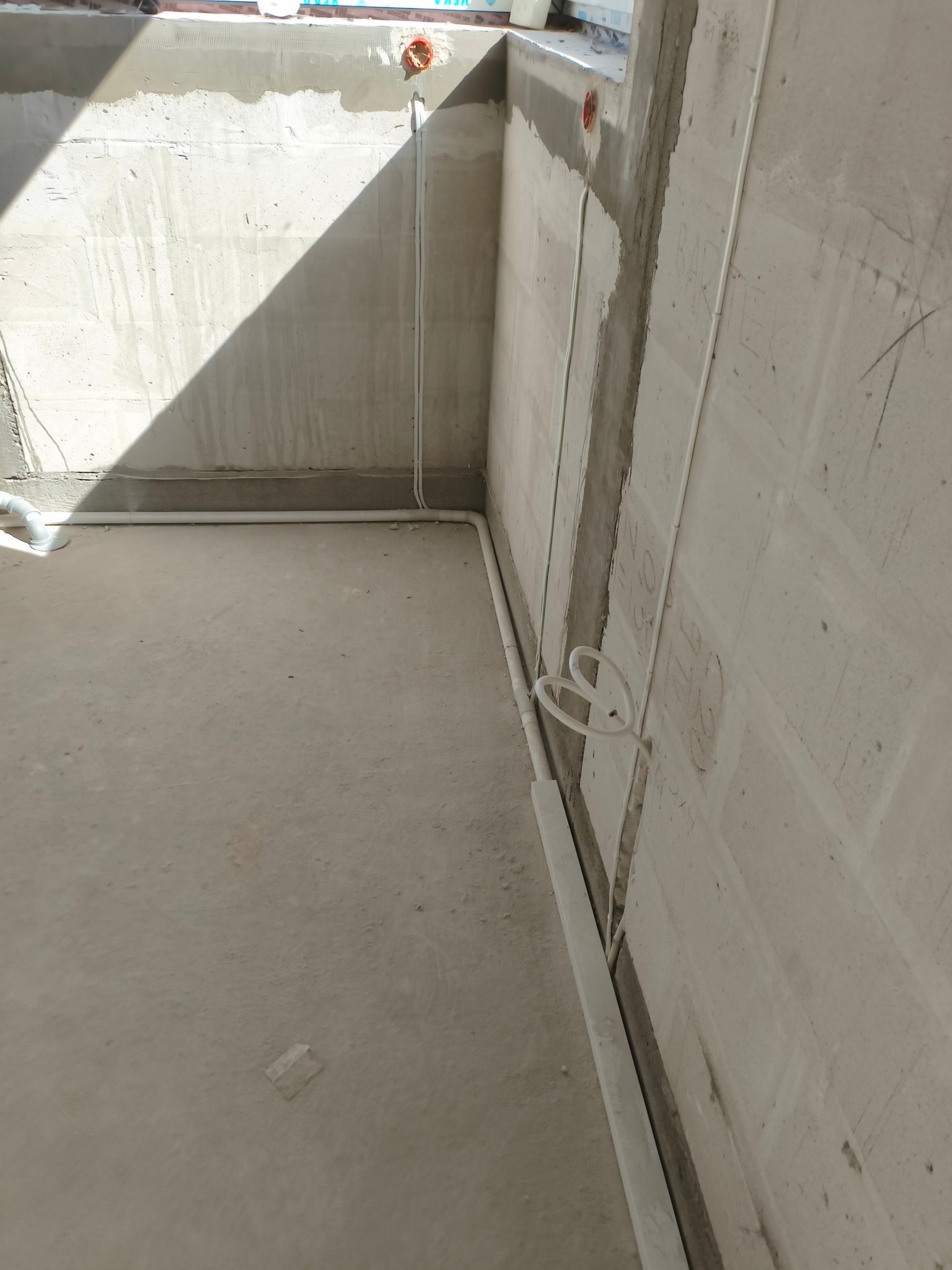 Surowy stan: białe kable elektryczne prowadzone wzdłuż ścian w nowym budynku, widoczne puszki instalacyjne i betonowe ściany w trakcie prac wykończeniowych.