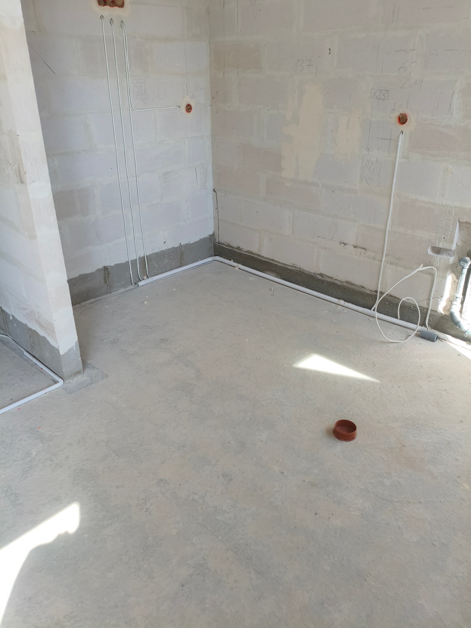 Surowy stan: białe ściany z widocznymi przewodami elektrycznymi w peszlach, przygotowane do dalszych prac wykończeniowych. Na podłodze leży element instalacji.