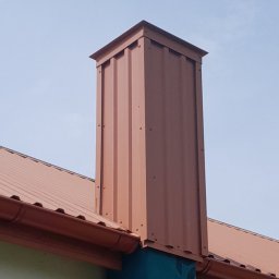 Dachy Paweł Wrzodak - Brązowy komin obłożony blachą trapezową, z widocznymi nitami, harmonizujący z dachem i rynną w tym samym odcieniu, na tle jasnego nieba.