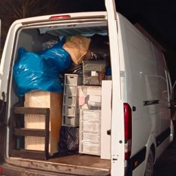 Mateusz Bujok - Wnętrze białego busa wypełnione po brzegi spakowanymi rzeczami, gotowe do transportu. Widoczne kartony, worki i plastikowe pojemniki.