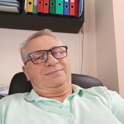 DN_DOREX - Zbigniew Szalc - Portret mężczyzny w okularach na tle biura z segregatorami. Ujęcie z dołu, podkreślające profesjonalizm i doświadczenie.