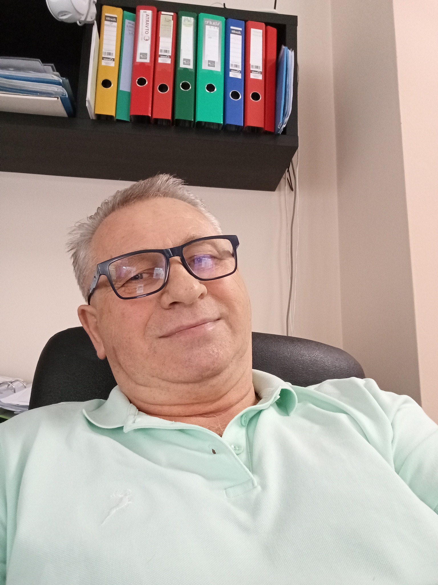 Portret mężczyzny w okularach na tle biura z segregatorami. Ujęcie z dołu, podkreślające profesjonalizm i doświadczenie.