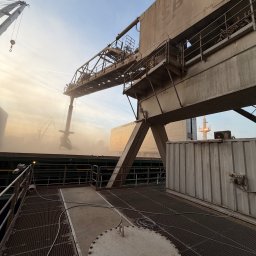 SpecMontSerwis Radosław Suchecki - Widok na suwnicę portową SBT w trakcie załadunku, z widoczną konstrukcją stalową i elementami infrastruktury przemysłowej w tle, w warunkach zapylenia.