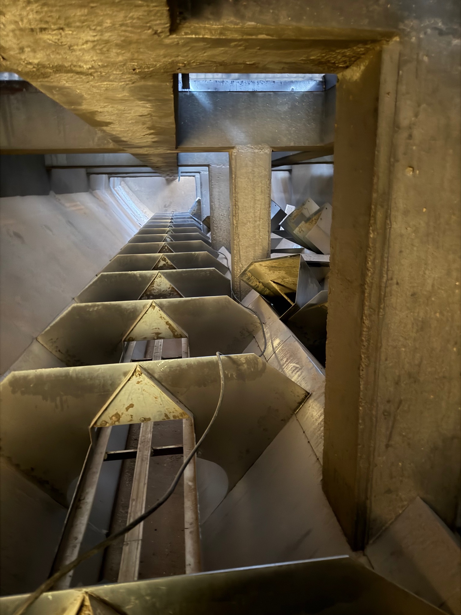 Wnętrze konstrukcji stalowej hali z perspektywy pionowej w Chrzanowie. Widoczne elementy nośne i schodkowe. Oświetlenie górne, surowy industrialny charakter.