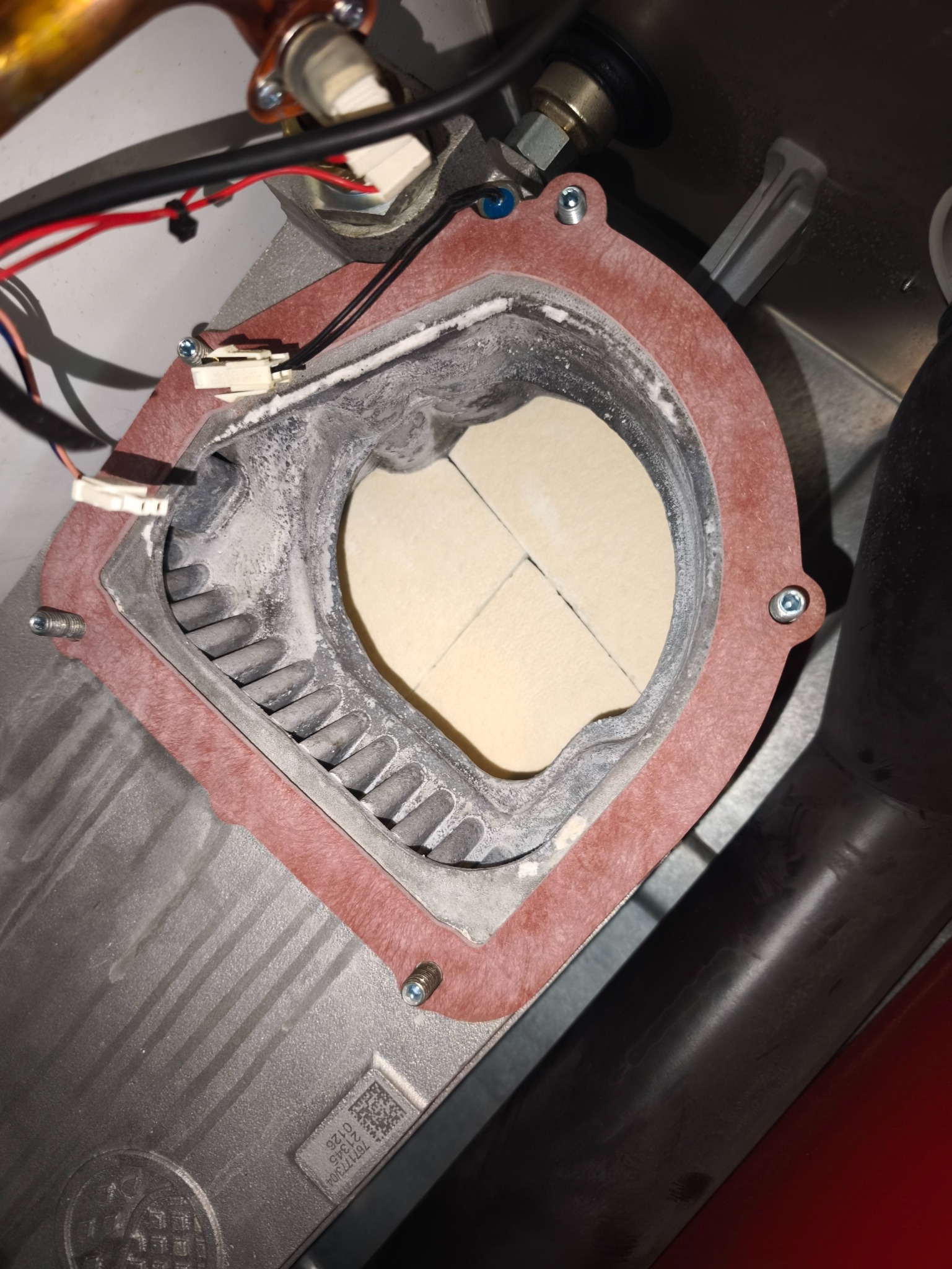 Wnętrze pieca gazowego z widocznym palnikiem i elementami instalacji. Widoczne ślady użytkowania i osad. Detaliczny widok na komponenty pieca.