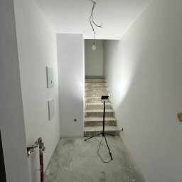 JMP Rzeszów - Wnętrze po malowaniu: białe ściany, schody w tle, widoczny sprzęt oświetleniowy i puszki z farbą. Minimalistyczny styl, surowe wykończenie.