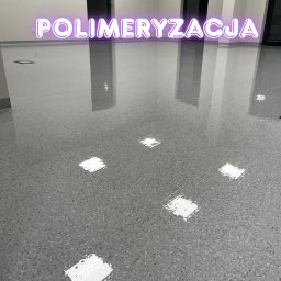 Clean My World - Błyszcząca, szara posadzka żywiczna z efektem lastryko w nowym biurze, odbijająca światło lamp i neonowy napis 'Polimeryzacja'. Widoczne dwie pary drzwi.